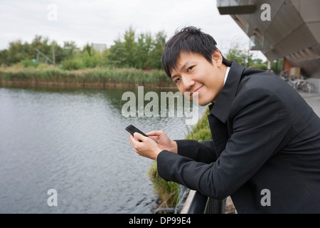 Portrait of happy businessman with cell phone leaning on bridge railing Banque D'Images