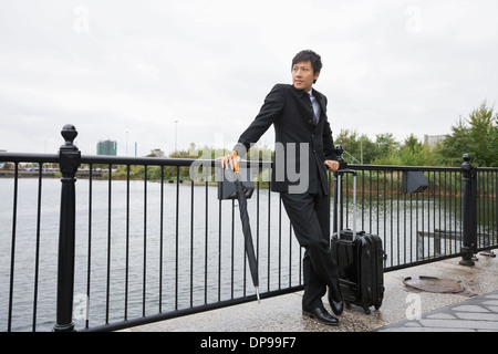 Toute la longueur du businessman with luggage leaning on railing le long de la rivière Banque D'Images