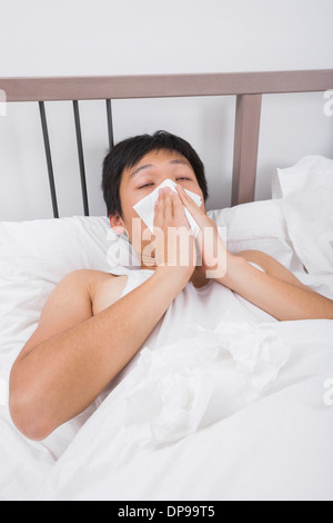 Asian man blowing nose in bed Banque D'Images