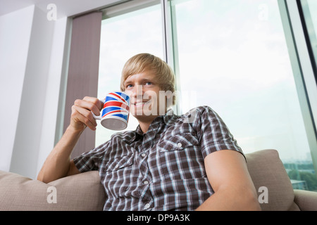 Thoughtful smiling Young man with coffee cup dans la salle de séjour à la maison Banque D'Images