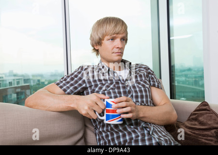 Thoughtful young man sitting with coffee cup dans la salle de séjour à la maison Banque D'Images