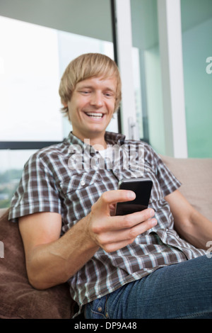 Cheerful mid-adult man text messaging on sofa at home Banque D'Images