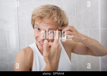 Portrait de l'homme presser bouton sur son front dans la salle de bains Banque D'Images