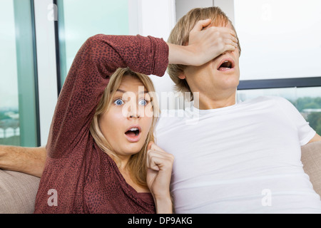 Femme choqué couvrant les yeux de l'homme en regardant la TV à la maison Banque D'Images