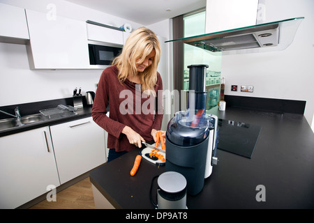 Young blonde woman chopping carrots on cutting board in kitchen Banque D'Images