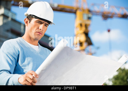 Male architect reviewing blueprint at construction site Banque D'Images