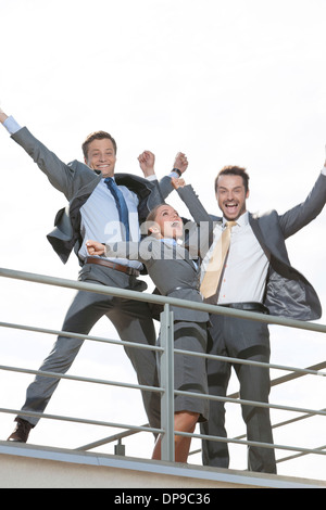 Low angle view of businesspeople excité avec bras levés debout sur terrasse contre ciel clair Banque D'Images