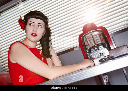 Belle jeune femme en robe rouge assis à table au restaurant Banque D'Images