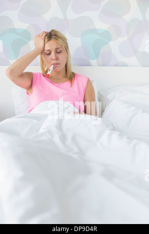 Femme prendre la température avec le thermomètre tout en souffrant de maux de tête Banque D'Images