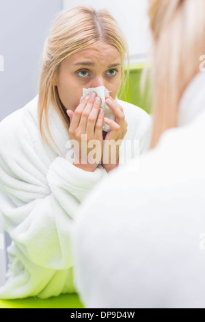 Young woman blowing nose dans du papier de soie en regardant mirror Banque D'Images