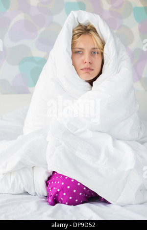 Portrait de jeune femme souffrant de la fièvre en l'enveloppant dans quilt in bed Banque D'Images