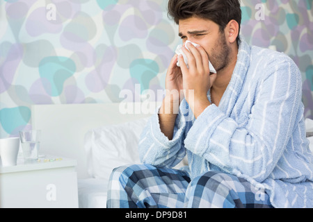 Homme malade soufflant son nez dans du papier de soie sur le lit chez lui Banque D'Images