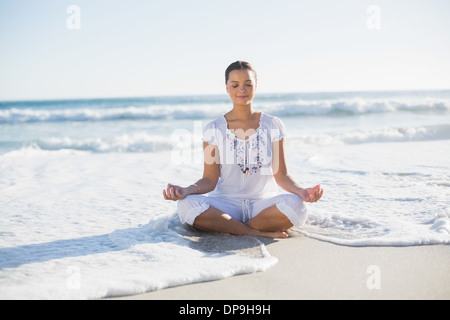 La jolie femme en position du lotus sur la plage avec des vagues atteignant sa Banque D'Images