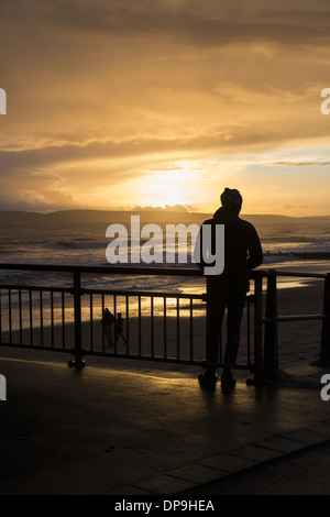 Silhouette d'homme debout sur la jetée de Boscombe et regardant le coucher du soleil à Dorset, Angleterre, Royaume-Uni Banque D'Images