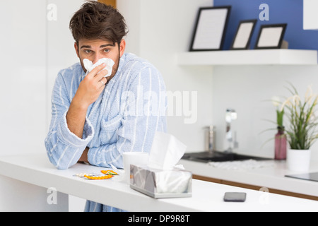 Les jeunes malades man blowing nose dans du papier de soie Banque D'Images