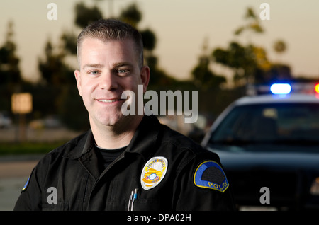 Un souriant et chaleureux à l'agent de police avec sa voiture de patrouille dans l'arrière-plan. Banque D'Images