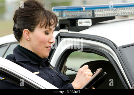 Une femme agent de police écrit un billet tout en vous tenant à côté de sa voiture de patrouille. Banque D'Images