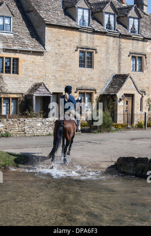 Un cheval-cavalier dans les Cotswolds village de Lower Slaughter équitation à travers la Ford. L'oeil de la rivière traverse le village. Banque D'Images