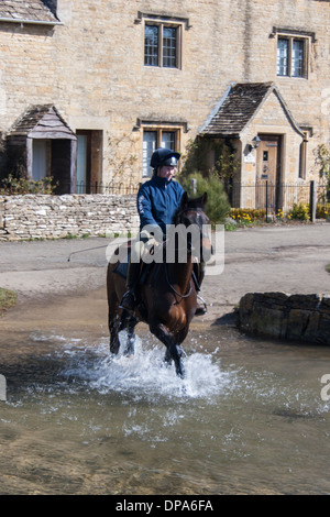 Un cheval-cavalier dans les Cotswolds village de Lower Slaughter équitation à travers la Ford. L'oeil de la rivière traverse le village. Banque D'Images