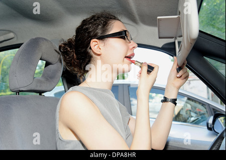 Young woman applying lipstick in car Banque D'Images