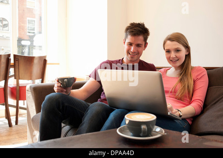 Jeune couple à la recherche à l'ordinateur personnel dans cafe Banque D'Images