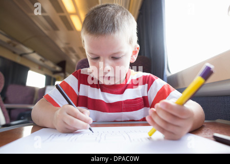 Jeune garçon avec un crayon, un stylo et du papier sur le train Banque D'Images