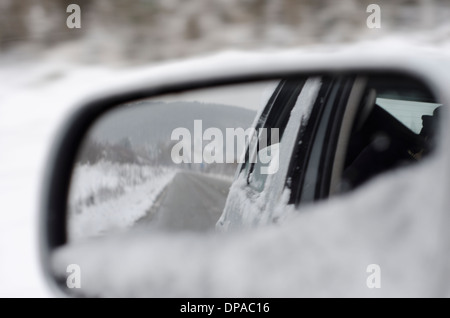 Collines couvertes de neige et de la route dans le rétroviseur d'une voiture Banque D'Images