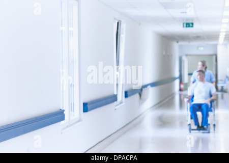 Nurse pushing patient in wheelchair down corridor Banque D'Images