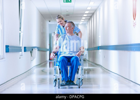 Nurse pushing patient in wheelchair down corridor Banque D'Images