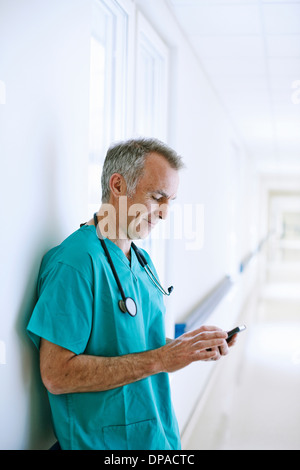 Surgeon standing in corridor looking at smartphone Banque D'Images
