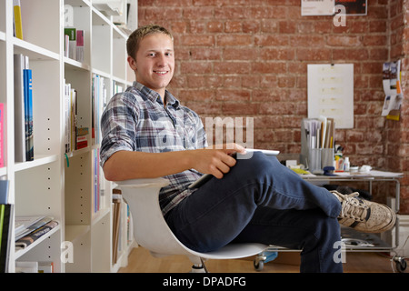 Portrait de jeune homme assis sur la chaise à l'aide d'une tablette numérique Banque D'Images