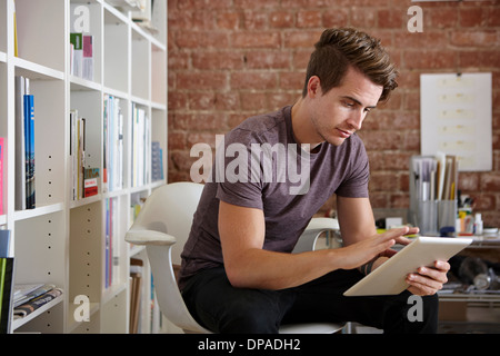 Portrait de jeune homme assis sur la chaise à l'aide d'une tablette numérique Banque D'Images