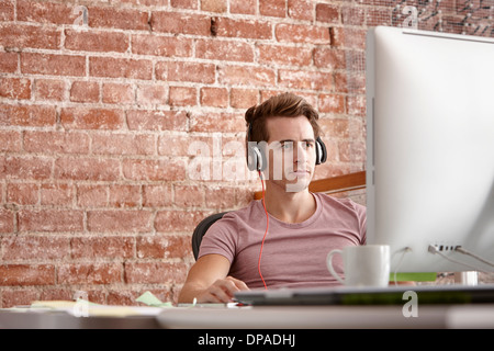 Jeune homme à l'aide d'ordinateur portant des écouteurs Banque D'Images