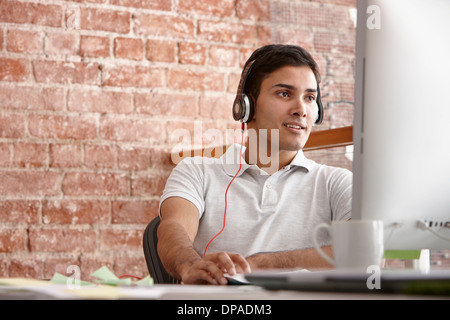 Jeune homme à l'aide d'ordinateur portant des écouteurs Banque D'Images