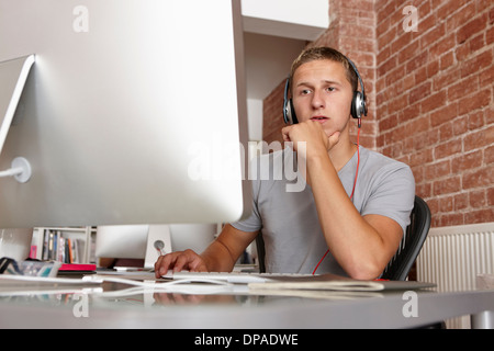 Jeune homme travaillant sur ordinateur portant des écouteurs Banque D'Images