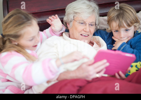Grand-mère et ses petits-enfants jouer jeu numérique au lit Banque D'Images