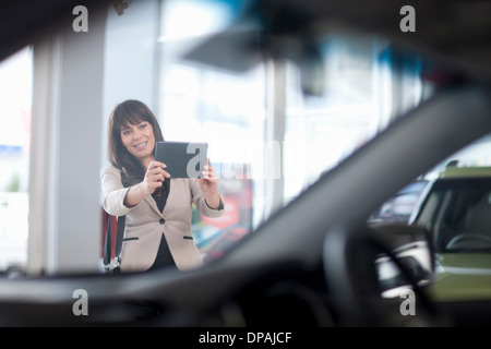 Young woman photographing car in showroom Banque D'Images