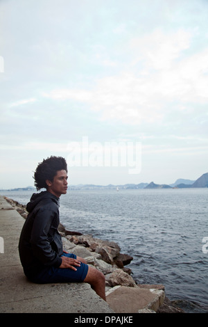Jeune homme assis sur le mur à la recherche en mer, Rio de Janeiro, Brésil Banque D'Images