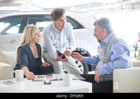 Car salesman talking to couple in car showroom Banque D'Images