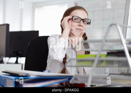 Girl wearing glasses with hand on chin in office Banque D'Images