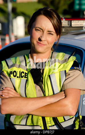 Une femme agent de police avec un froncement sur son visage alors qu'elle croise les bras devant elle partrol voiture. Banque D'Images