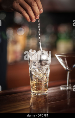 Barman en remuant Martini dans un verre à mélange avec des glaçons, tourné sur place sur une barre en bois. Banque D'Images