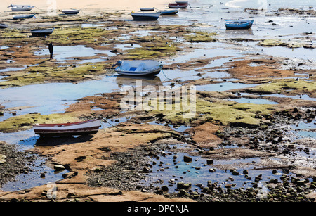 Cadix, Espagne. Figure solitaire parmi les petits bateaux de pêche sur la plage à marée basse. Banque D'Images