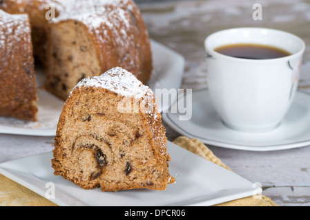 Tranche de gâteau bundt maison aux pruneaux et d'épices. Tasse de café et des gâteaux sur l'arrière-plan. Banque D'Images