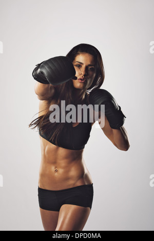 Portrait d'une jeune femme boxer de jeter un coup à l'appareil photo tout en pratiquant sur fond gris. Athlète féminine course mixte Banque D'Images