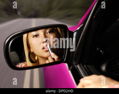 Young pretty asian woman applying lipstick dans une voiture sur une route, à la recherche dans un rétroviseur. Concept La distraction au volant. Banque D'Images