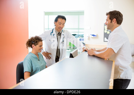 L'équipe médicale travaillant sur ordinateur tandis que l'Homme debout à la réception Banque D'Images