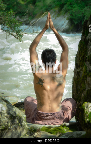 Un jeune homme se pratique le yoga et la méditation dans une paisible forêt himalayenne sur les rives d'un ruisseau de montagne sauvage. Banque D'Images