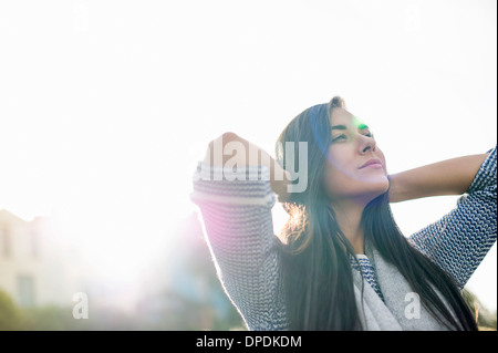 Jeune femme avec les mains derrière la tête dans la lumière du soleil Banque D'Images