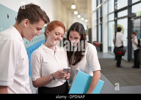 Les adolescents looking at mobile phone in school corridor Banque D'Images